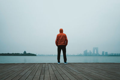 Rear view of man standing on pier over lake against sky