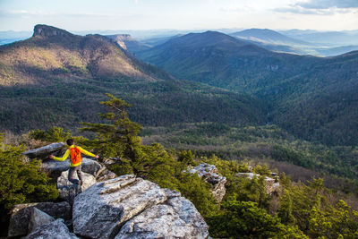 High angle view of man jumping on rock against landscape and sky