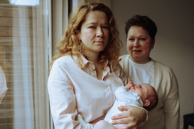 Portrait of smiling young woman holding baby standing in front of her mother