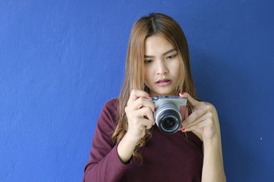 Young woman photographing while standing against blue wall