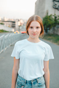 Red-haired teenager girl in a white t-shirt and jeans walks around the city. evening walks 