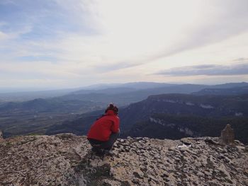 Woman crouching on landscape against sky