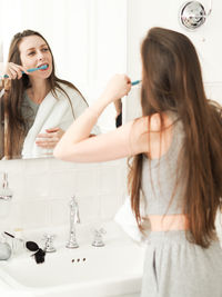  young woman with braces, standing in front of the mirror in the bathroom and brushing her teeth.