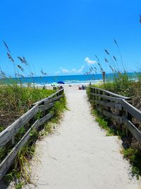 Walkway leading towards beach against sky