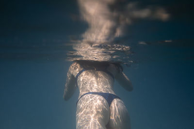 Woman swimming underwater in the ocean in clear blue water.