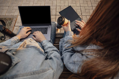 Close-up of hands of a man and a woman working using laptop, tablet, sitting on bench in park