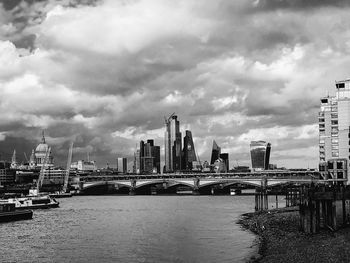 Bridge over river by buildings against sky in city