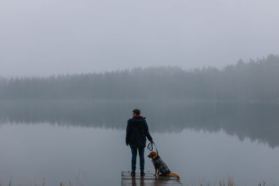 Man with dog standing on lake against sky