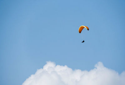 Low angle view of people paragliding against blue sky