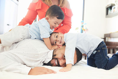 Positive hispanic couple with cute little sons gathering on bed and looking at camera while enjoying pastime at home