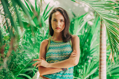 Portrait of young woman with arms crossed standing by trees