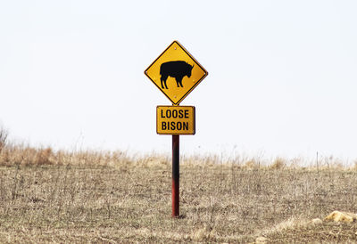 Road sign on field against clear sky