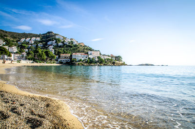 Low angle view of town on hill by sea against sky