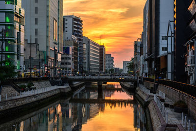 Bridge over river by buildings against sky during sunset