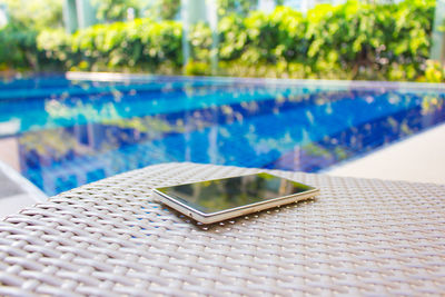 Close-up of mobile phone with swimming pool in background