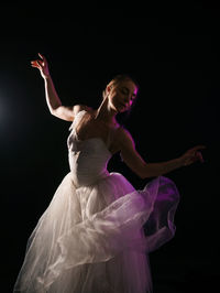 Ballet dancer wearing white dress dancing against black background