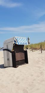 Hooded chairs on beach against blue sky