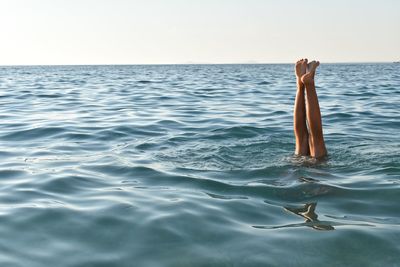 Low section of woman swimming in sea against clear sky during sunset