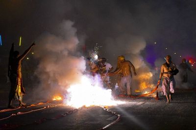 Men with firework exploding on road at night during festival