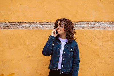 Young woman standing against yellow wall