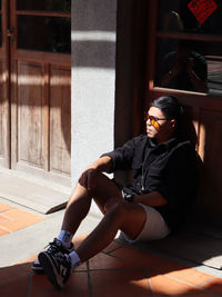 Full length of young man wearing sunglasses sitting againt the wall