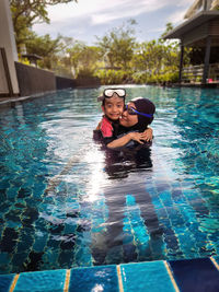 Smiling mother and her adorable little daughter hugging each other in a swimming pool.