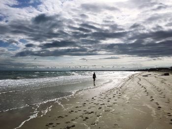 Silhouette person standing on beach against clouds