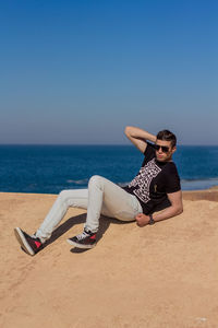 Man wearing sunglasses on beach against clear sky