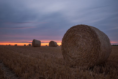 Hay bales on field against sky during sunset