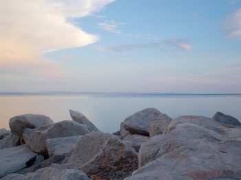 Scenic view of stones next to sea against cloudy sky