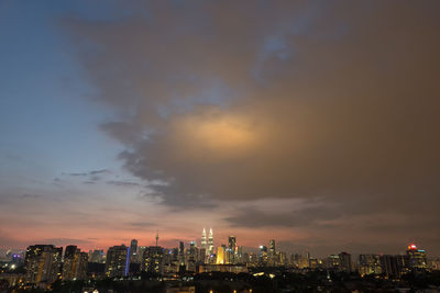 Illuminated cityscape against cloudy sky