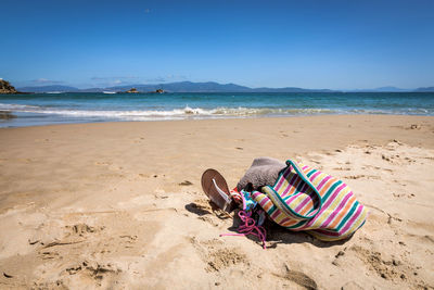 Personal accessories on sand at beach against blue sky