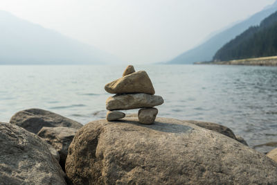 Stack of stones on rock by sea against sky