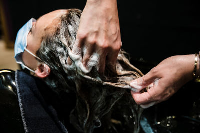 Cropped hand of hairdresser washing hair of client wearing flu mask