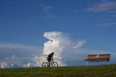 Man riding bicycle on field against sky