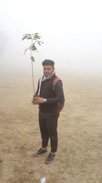 Full length portrait of young man standing on field against sky