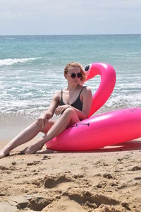Young woman sitting on shore at beach against sky