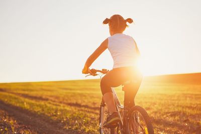 Rear view of girl riding bicycle on field against clear sky