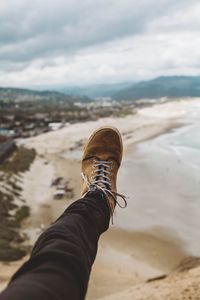 Low section of man wearing shoe against beach
