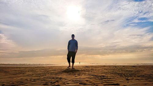 Rear view of man standing on beach against sky during sunset