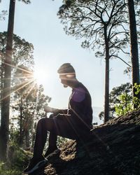 Side view of young man sitting on tree trunk