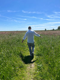 Rear view of man standing on field against sky