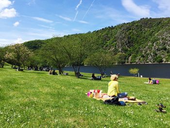 People on grassy field by river against sky