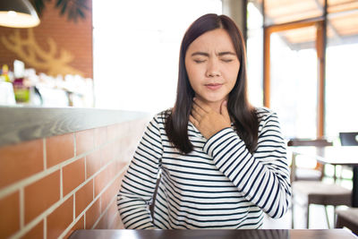 Young woman suffering from neck pain while sitting in restaurant