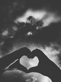Low angle view of person hand heart shape against sky