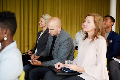 Male entrepreneur writing while sitting with colleagues in seminar at workplace