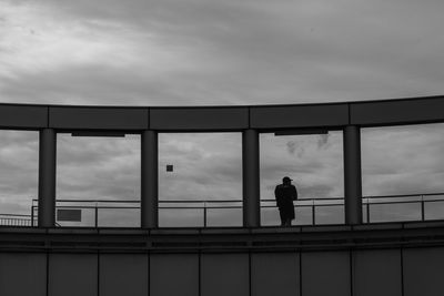 Silhouette man standing by railing against sky