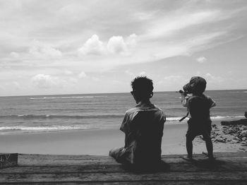 Rear view of father and son on pier at beach against sky