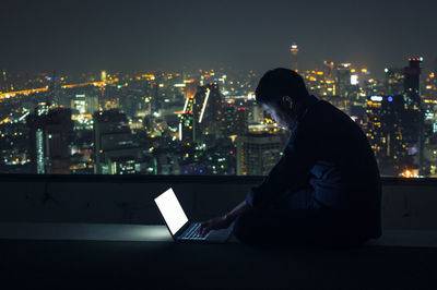 High angle view of woman sitting in illuminated building against sky at night