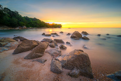 Rocks on shore against sky during sunset